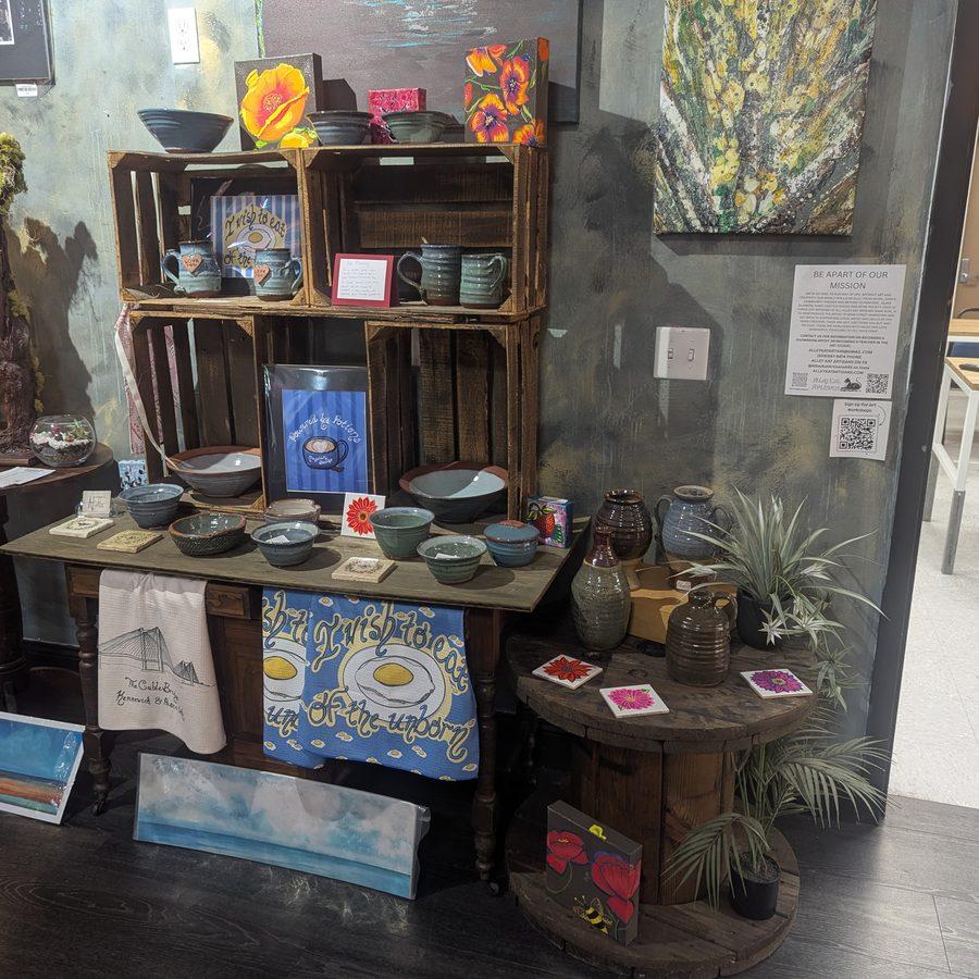 Handmade pottery bowls on wooden crates alongside original paintings on a textured wall